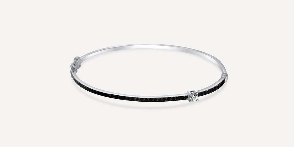 A striking white gold pavé-set melee black diamond bracelet bangle infused with a gleaming square-cut white diamond. The designer's signature bangle distinguishes itself from other bangles to better mix and match. Wear separately or in enhanced layering, the bracelet captivates glare.  Estimated Diamond Weight: 0.97 Carat Of Diamond  Gold Weight: 18K White Gold