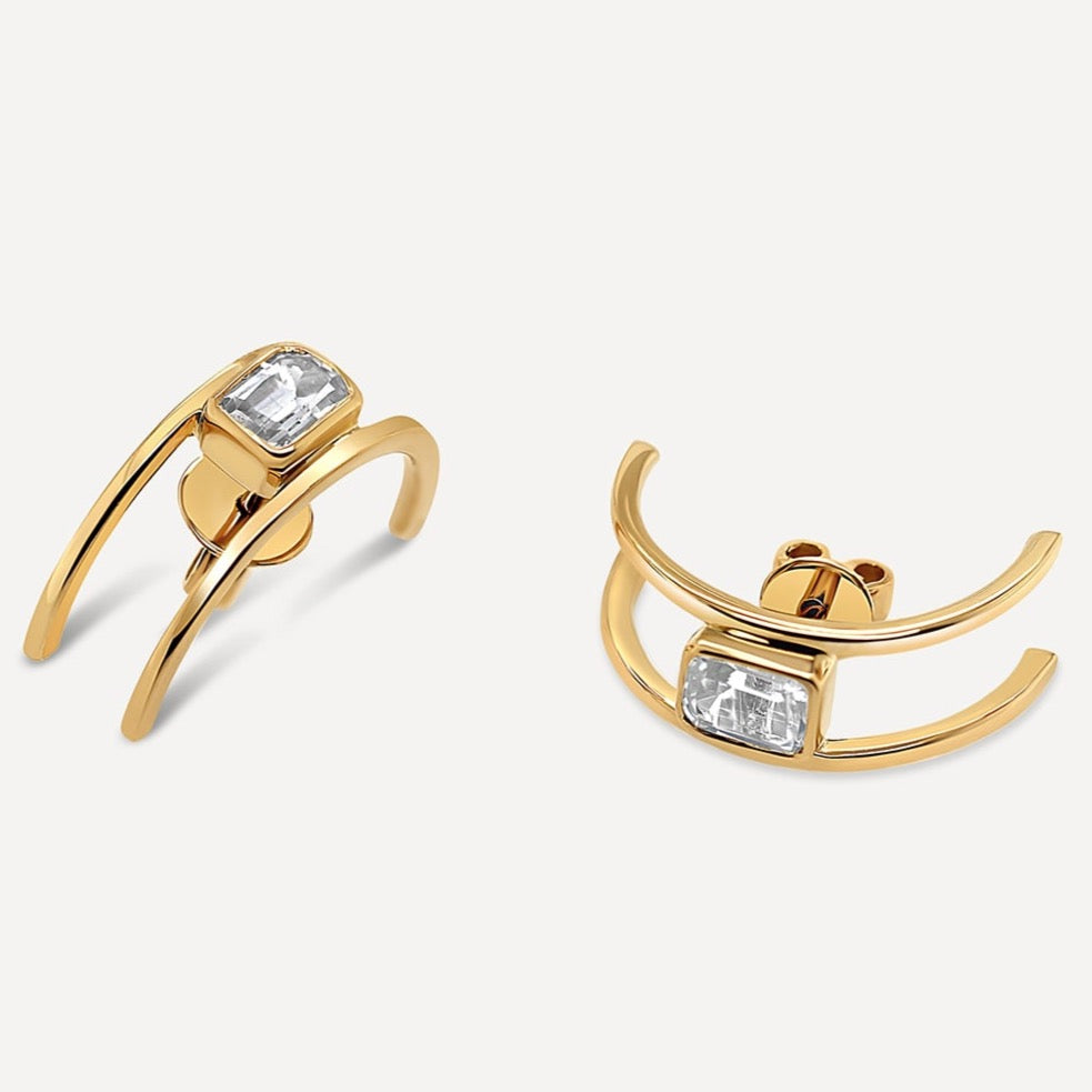 Yellow gold earrings designed to represent two gold rails holding in between one emerald-cut white sapphire. The ideal gift to someone who appreciates chic boldness.   Estimated Diamond Weight:1.33 carat of sapphire Gold Weight:18K Yellow gold