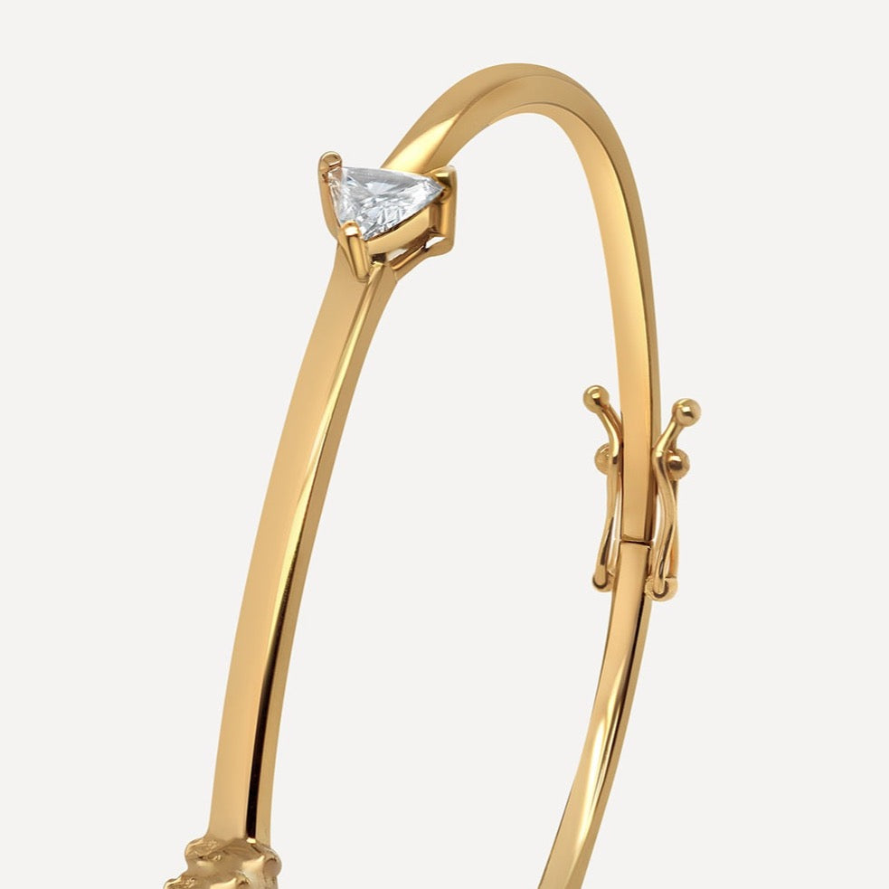 A striking yellow gold bracelet bangle infused with a gleaming triangle-cut white diamond. The designer's signature bangle distinguishes itself with from other bangles to better mix and match. Wear separately or layered, the bracelet captivates glare.  Estimated Diamond Weight: 0.16carat of diamond Gold Weight: 18k Yellow gold